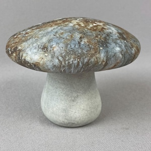 May include: A decorative mushroom sculpture featuring a smooth, rounded cap with a marbled pattern of brown, gray, and white tones. The stem is a solid, light gray color with a matte texture, supporting the wide, curved cap in a balanced form.