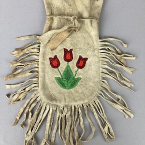 May include: A cream-colored leather pouch with a drawstring closure and long fringe. The front features a beaded design of three red tulips with green leaves. The pouch is likely handmade and has a rustic, vintage aesthetic.