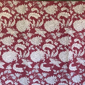 May include: A red and white floral patterned quilt. The quilt features a repeating design of large, stylized flowers and foliage in white against a deep red background. The pattern is evenly distributed across the fabric.