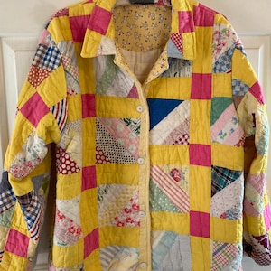 May include: A yellow quilted jacket with pink and white patchwork squares. The jacket has a button-up front and long sleeves.
