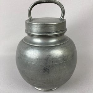 May include: A silver pewter jar with a lid and a handle. The jar has a rounded body and a slightly flared lip.