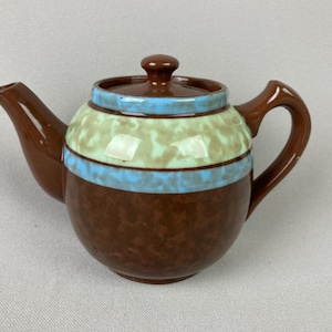 May include: A brown ceramic teapot with a rounded body, spout, and handle. The teapot features a light blue and green band around the middle, with a brown lid and knob. The teapot is designed for brewing tea.
