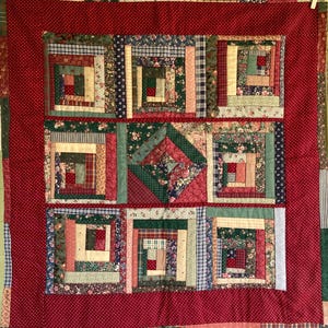 May include: A handmade quilt with a red border and a patchwork design. The quilt features squares with various patterns, including floral, plaid, and solid fabrics in shades of red, green, and cream. The quilt's dimensions are approximately 60 inches by 60 inches.