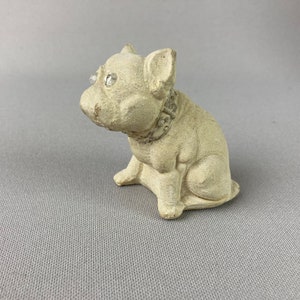 Pu&ograve; includere: Una piccola statuetta in ceramica bianca di un bulldog francese con un collare gioiello. La statuetta ha un aspetto realistico e occhi di strass scintillanti.