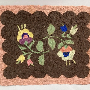 May include: A rectangular, hand-hooked rug with a scalloped edge. The rug features a dark brown center with a floral design in yellow, purple, pink, blue, and green. The border is a light peach color.