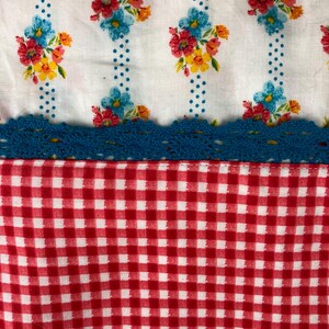 May include: A white fabric with a blue and white floral pattern and blue polka dots. The fabric has a blue crocheted trim and a red and white gingham pattern at the bottom.