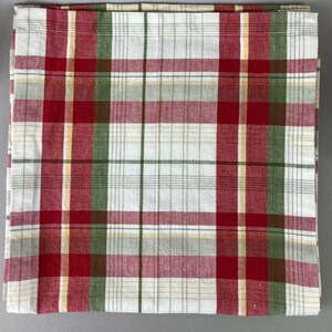 May include: A folded white, red, green, and yellow plaid tablecloth. The plaid pattern is made up of intersecting vertical and horizontal lines. The tablecloth is made of a woven fabric.
