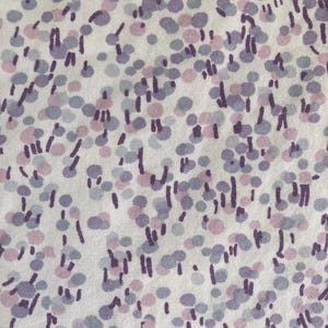 May include: Close-up of a white fabric with a repeating pattern of purple, lavender, and light pink dots and short vertical lines. The design is scattered across the fabric, creating a textured appearance. The fabric appears to be cotton or a similar material.