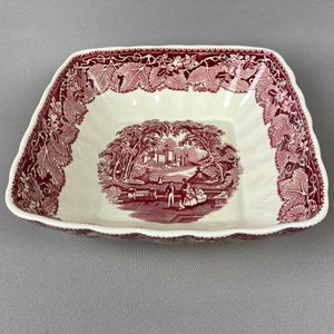 May include: A square, white ceramic serving bowl with a scalloped edge. The bowl is decorated with a pink floral pattern and a scene of a country landscape with a bridge and people.