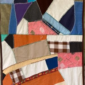 May include: A handmade crazy quilt featuring a patchwork of various fabric scraps in colors including orange, pink, blue, white, brown, and black. The pieces are joined with visible decorative cross-stitching in contrasting thread colors.