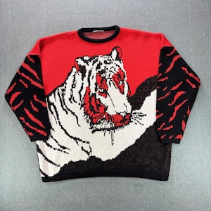 Puede incluir: Un suéter de punto de manga larga con un gráfico grande de un tigre blanco en la parte delantera. El suéter tiene una sección superior roja, un cuello redondo negro y mangas negras con patrones de rayas de tigre rojas. La parte inferior es negra.