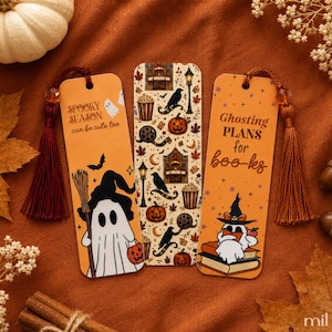 May include: Three rectangular bookmarks with rounded corners. The left one is orange with a ghost holding a broom and pumpkin, reading "SPOOKY SEASON can be cute too". The centre one has a pattern of pumpkins, crows, and popcorn. The right one is orange with a ghost reading on books, reading "Ghosting PLANS for boo-ks". Each has a tassel.