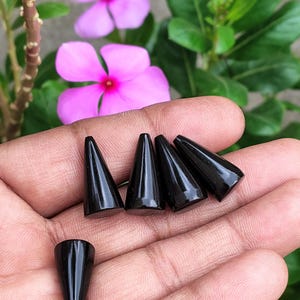 May include: Five smooth, polished black cone-shaped objects with a glossy finish. Four of the cones are arranged in a horizontal row, while one single cone is positioned separately below them, all featuring a pointed tip and a flat circular base.