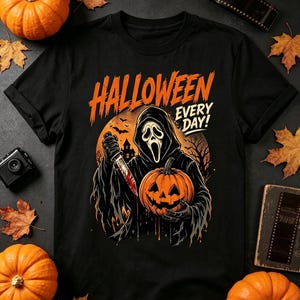 Può includere: Una t-shirt nera con la grafica di una figura incappucciata con maschera bianca che tiene in mano un coltello e una zucca. Il testo HALLOWEEN EVERY DAY! è stampato in arancione sopra la figura, davanti a una grande luna arancione.