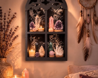 May include: A black wall-mounted shelf with a gothic arch top and four compartments. The back panels feature a black and white floral pattern. The shelf holds various crystal points, clusters, spheres, and small lit candles on each level.