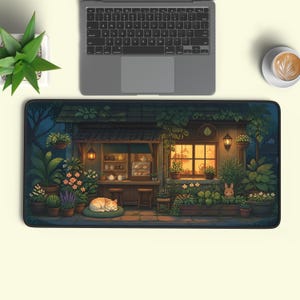 May include: A rectangular desk mat featuring a detailed illustration of a cosy, plant-filled shop exterior at night. A ginger cat sleeps on a green cushion near the entrance, while a small rabbit sits among potted plants and warm glowing lanterns.