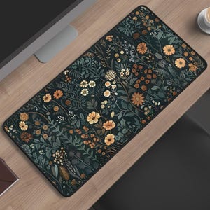 Peut inclure: Un tapis de bureau rectangulaire présentant un fond sombre avec un motif dense et répétitif de fleurs sauvages et de feuillage dans des tons orange, jaune, blanc et vert sourd. Le tapis a des coins arrondis et une bordure cousue noire.