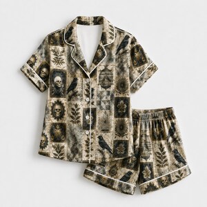May include: A short-sleeve button-down pajama shirt and matching shorts set featuring a patchwork print of black crows, human skulls, birdcages, and botanical leaf patterns in shades of black, gold, and beige with white piping trim.