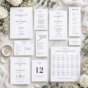 May include: A collection of white wedding stationery featuring black serif and script typography. The set includes a welcome sign, details card, invitation, menu, RSVP postcard, thank you note, place card, save the date, table number 12, and seating chart.