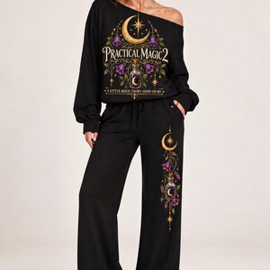 May include: A black long-sleeve off-the-shoulder top and matching wide-leg pants set. The top features a graphic with a crescent moon, purple flowers, a potion bottle, and the text "PRACTICAL MAGIC 2 A LITTLE MAGIC LOOKS GOOD ON ME."