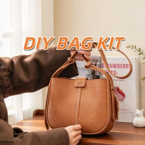 Puede incluir: Un bolso tipo cubo de color canela con superficie texturizada, que presenta una costura vertical blanca en el centro, un cierre de solapa con un pequeño logotipo en relieve y una correa ajustable. El texto DIY BAG KIT es visible.