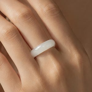 May include: A smooth, solid white band ring with a polished, glossy finish. The ring features a simple, rounded profile and a uniform, opaque white color throughout the entire circular band, creating a clean and understated appearance on the finger.