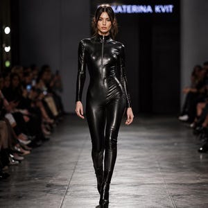 May include: A long-sleeved, black, form-fitting jumpsuit with a high collar and a full-length front zipper. The garment features a glossy, reflective finish that contours to the body, extending down to the ankles with matching black footwear.