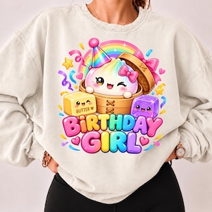 Op de afbeelding: Een beige sweater met ronde hals voorzien van een afbeelding van een schattige dumpling in een bamboe stoommandje met een feesthoedje, vergezeld door een blokje boter en een paars blokje, met de tekst "BIRTHDAY GIRL" in kleurrijke letters.