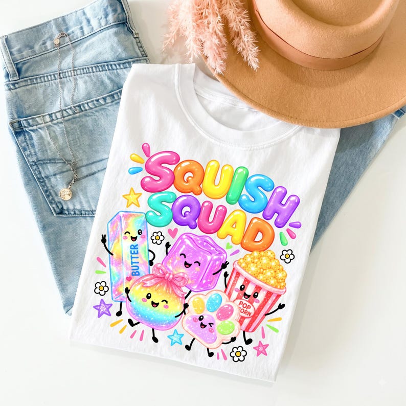 Op de afbeelding: Een wit t-shirt met de kleurrijke tekst "SQUISH SQUAD" boven cartoonillustraties van een pakje boter, een paarse kubus, een regenboogkleurig rond object, een pootafdruk en een popcornemmer, allemaal met lachende gezichtjes en ledematen.