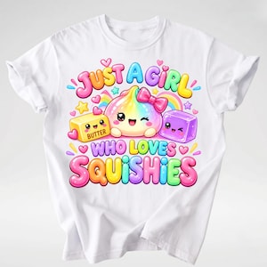 Op de afbeelding: Een wit t-shirt met een kleurrijke afbeelding van een regenboogkleurig figuurtje met een roze strik, een geel blokje boter met het label BUTTER en een paarse kubus. De tekst luidt JUST A GIRL WHO LOVES SQUISHIES in vrolijke, ronde letters.