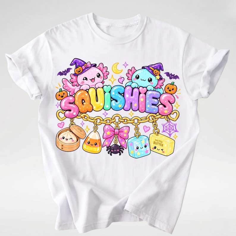 Op de afbeelding: Een wit t-shirt met een kleurrijke afbeelding van twee axolotls met heksenhoeden boven het woord SQUISHIES in bubbelletters. Daaronder hangt een gouden ketting met bedeltjes zoals een dumpling, maissnoepje, roze strik, spin, kubus en een blokje boter.