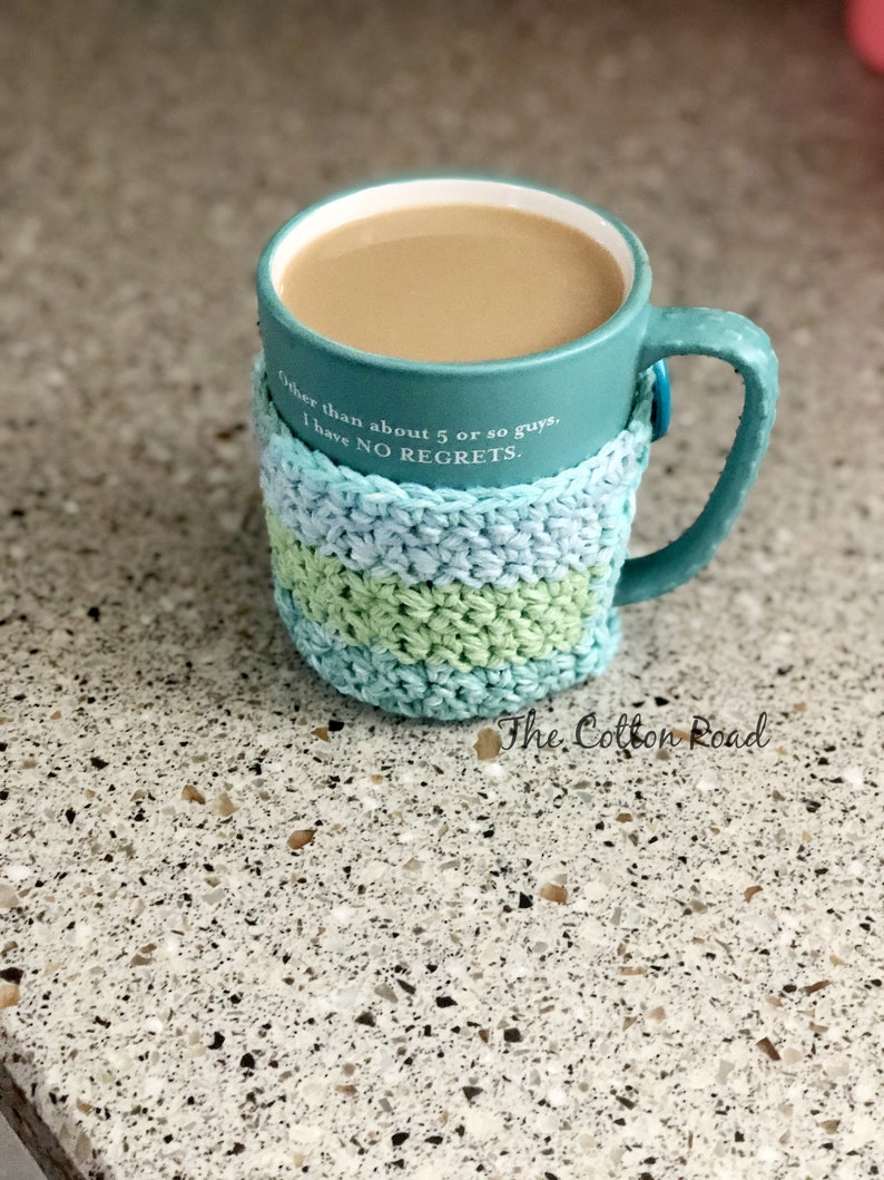 May include: A teal mug with a crocheted cozy in shades of blue and green. The mug has a quote that reads "Other than about 5 or so guys, I have NO REGRETS." The mug is sitting on a speckled countertop.