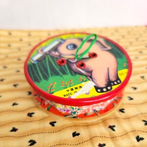 May include: A vintage red and yellow thread spool with a cartoon elephant design. The spool has a green elastic band and the text "MADE IN" and Chinese characters.