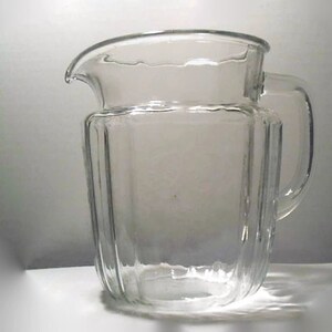 May include: A clear glass pitcher with a ribbed design and a handle. The pitcher is empty.