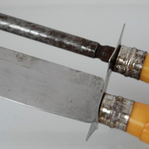 May include: A set of two vintage knives with yellow plastic handles and silver metal accents. The knives have a silver blade and a steel sharpening rod.