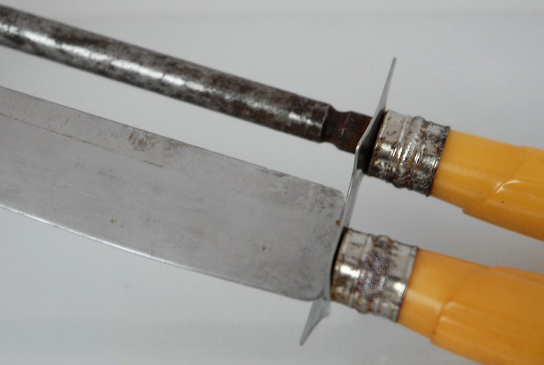 May include: A set of two vintage knives with yellow plastic handles and silver metal accents. The knives have a silver blade and a steel sharpening rod.