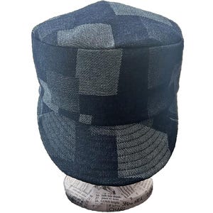 K&ouml;nnte beinhalten: Eine M&uuml;tze im Milit&auml;rstil mit einem Patchwork-Design aus dunkelblauen und anthrazitfarbenen Denim-Stoffquadraten. Die Kopfbedeckung hat eine flache Oberseite, eine strukturierte Krone und einen kurzen, steifen Schirm aus strukturiertem Denim.
