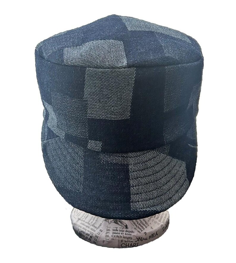 K&ouml;nnte beinhalten: Eine M&uuml;tze im Milit&auml;rstil mit einem Patchwork-Design aus dunkelblauen und anthrazitfarbenen Denim-Stoffquadraten. Die Kopfbedeckung hat eine flache Oberseite, eine strukturierte Krone und einen kurzen, steifen Schirm aus strukturiertem Denim.