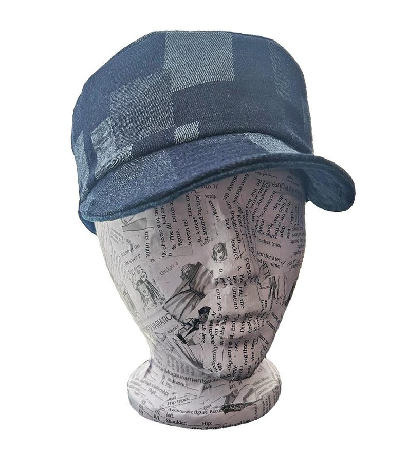 K&ouml;nnte beinhalten: Eine dunkelblaue Cadet-M&uuml;tze mit einem dezenten Karomuster auf der Krone und dem Schirm. Die Kopfbedeckung hat ein strukturiertes Design mit flacher Oberseite und einem kurzen, gebogenen Schirm, gefertigt aus einem strukturierten marineblauen Stoff.