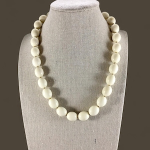 May include: A white oval bead necklace on a fabric-covered mannequin.