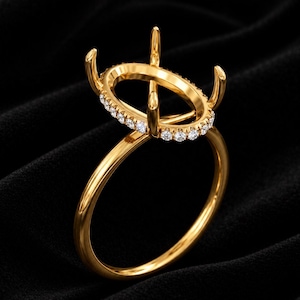 May include: A gold ring setting featuring an oval-shaped head with four prongs designed to hold a gemstone. The band and the oval gallery are crafted from polished yellow gold, with the gallery accented by a row of small, round, clear stones.