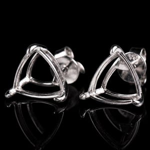 Puede incluir: Un par de monturas para pendientes de metal color plata con un diseño de tres garras triangulares. Cada montura tiene tres garras para sujetar una piedra preciosa, con un poste trasero y un pequeño sello 925 en la base del pendiente.