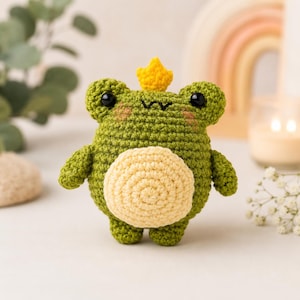 Puede incluir: Un pequeño peluche de rana tejido a ganchillo, de forma redonda y color verde, con una corona amarilla en la cabeza, una mancha circular de color amarillo claro en el vientre, ojos de plástico negro y una boca cosida con hilo.