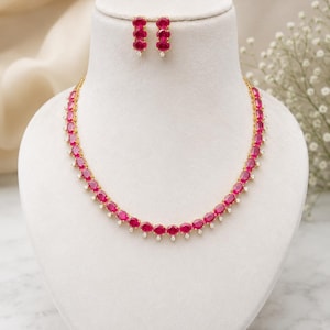 May include: A gold-toned necklace and matching earring set featuring oval-cut vibrant pink stones arranged in a continuous line, with each stone accented by a small, clear, round-cut white stone at the base of the setting.