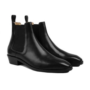 May include: A pair of black leather Chelsea boots featuring a smooth finish, rounded toes, and black elastic side panels. Each boot has a pull tab at the top of the heel collar and a low, stacked block heel with a black outsole and stitching.