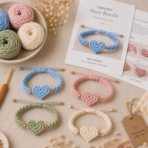 Könnte beinhalten: Vier verstellbare Häkelarmbänder mit Herzmotiv in Hellblau, Rosa, Salbeigrün und Creme, jeweils mit einem zentralen Herz und goldfarbenen Perlen. Enthält eine 4,5-mm-Häkelnadel, Garnknäuel, eine gedruckte Anleitung und ein braunes Papieretikett.
