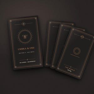 Könnte beinhalten: Ein Satz schwarzer Tarotkarten mit kupferfarbenen geometrischen Linien. Die Schachtel zeigt den Text UMBRA & ORE, EDITION III - OILY MOTH und 22 CARDS + GUIDEBOOK. Eine Karte zeigt einen Kreis und den Text THE WORLD, The Ring.