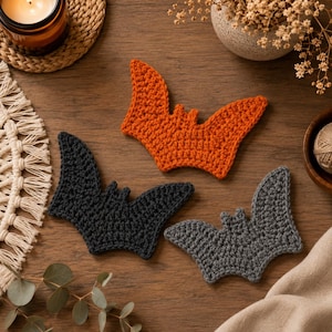 Può includere: Tre sottobicchieri all'uncinetto a forma di pipistrello nei colori arancione, nero e grigio scuro. Ogni sottobicchiere presenta un design testurizzato cucito a mano con ali appuntite e piccole orecchie.