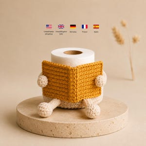 Puede incluir: Un rollo de papel higiénico blanco con una funda de ganchillo que muestra un libro de color amarillo mostaza sostenido por dos pequeños brazos de ganchillo color crema y dos piernas de ganchillo color crema en la base.