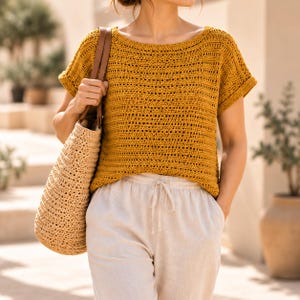 May include: A mustard yellow short-sleeved crochet top with a horizontal open-stitch pattern, paired with light beige drawstring trousers and a large, textured, light tan woven straw tote bag with brown leather shoulder straps.